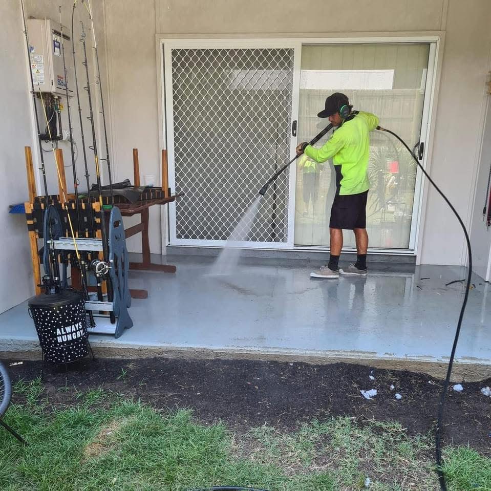 Michael uses a pressure washer to clean a concrete patio in front of a sliding glass door in Caboolture
