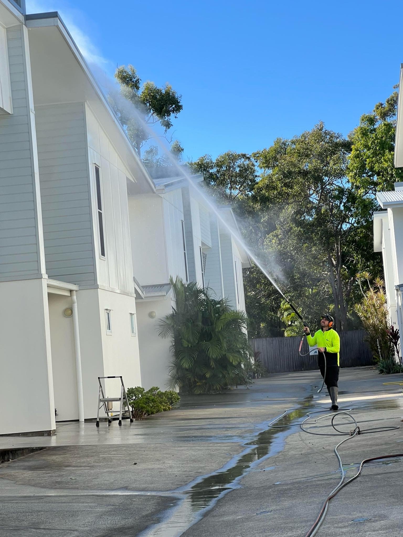 Michael, in a yellow shirt, uses a high-pressure hose to expertly clean a light house exterior—property maintenance in Brisbane.
