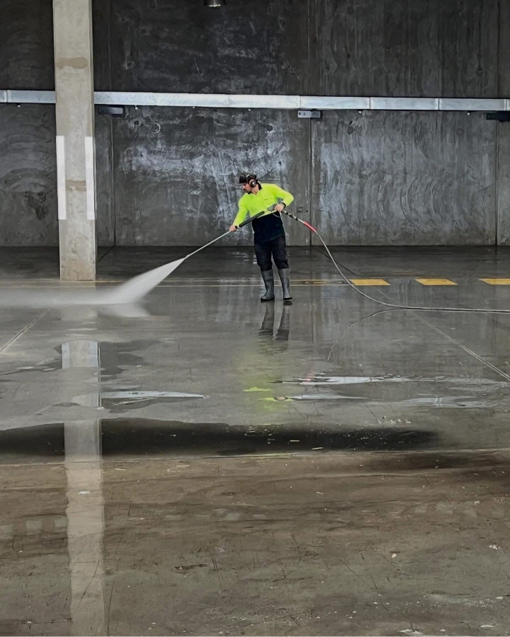 Michael in a neon yellow shirt pressure washing the concrete floor of an empty industrial building in Moreton Bay.