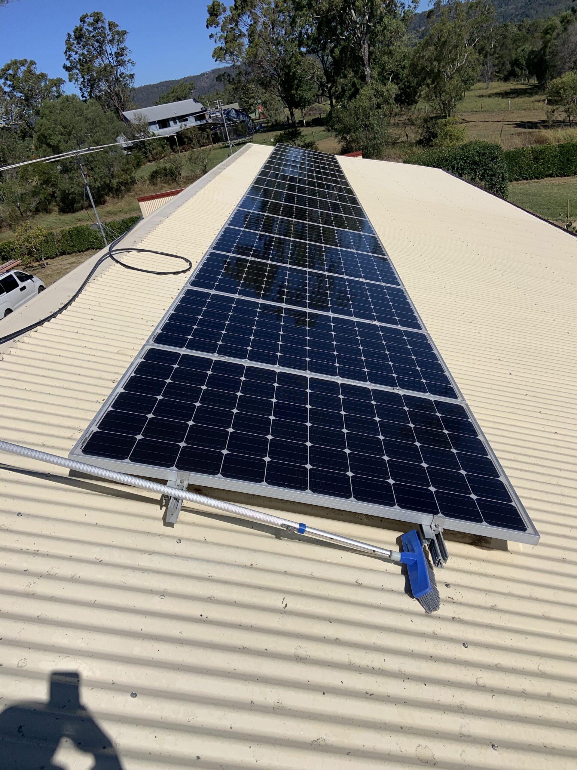 A row of solar panels on a sloped metal roof in sunny Brisbane with trees in the background, ideal for regular Solar Panel Cleaning.