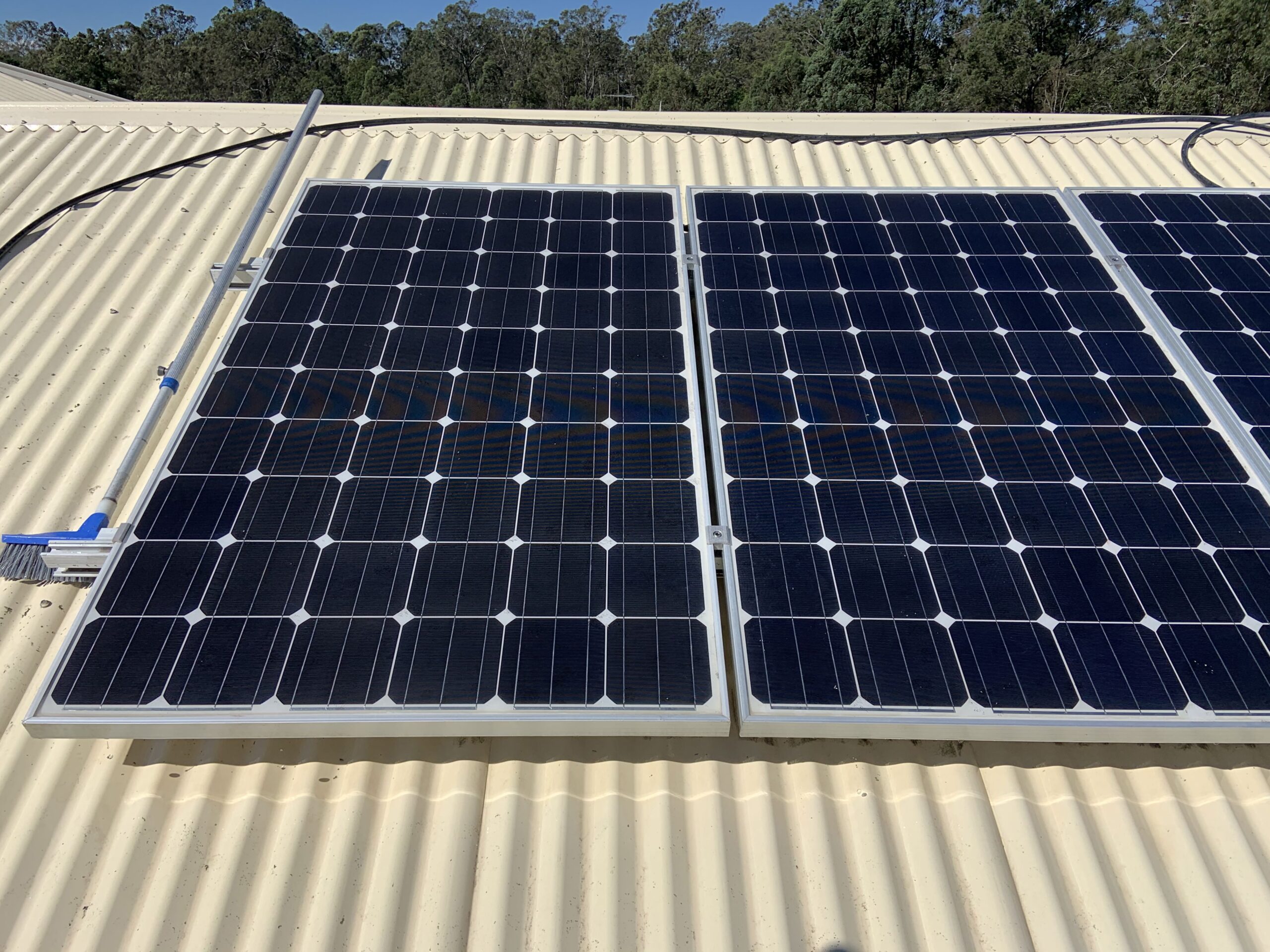 Two solar panels on a corrugated metal roof in Queensland with trees in the background, ideal for solar panel cleaning.