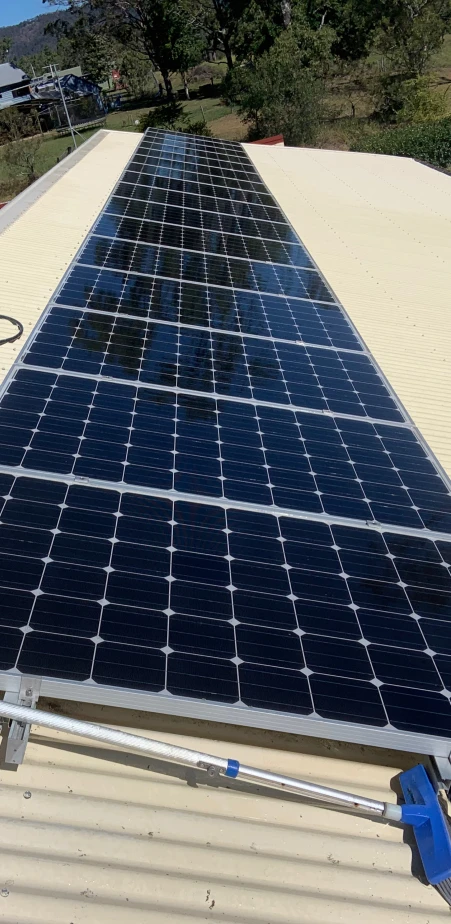 A row of solar panels on a sloped metal roof in Sunshine Coast with trees in the background, ideal for regular Solar Panel Cleaning.