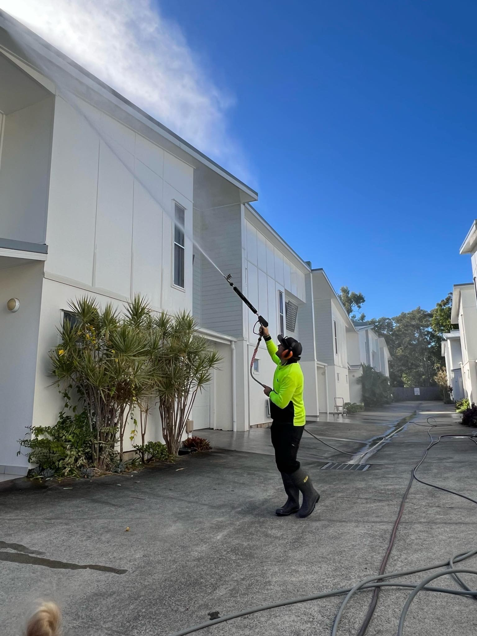 Michael in safety gear pressure washes the white exterior of a multi-story building, expert property maintenance in Brisbane Newstead.