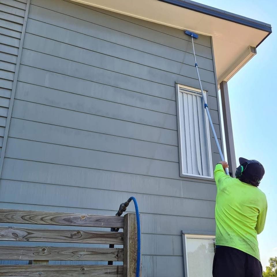 Michael in a high-vis shirt expertly cleans upper house walls and eaves with a long pole, property maintenance in Brisbane Chermside West