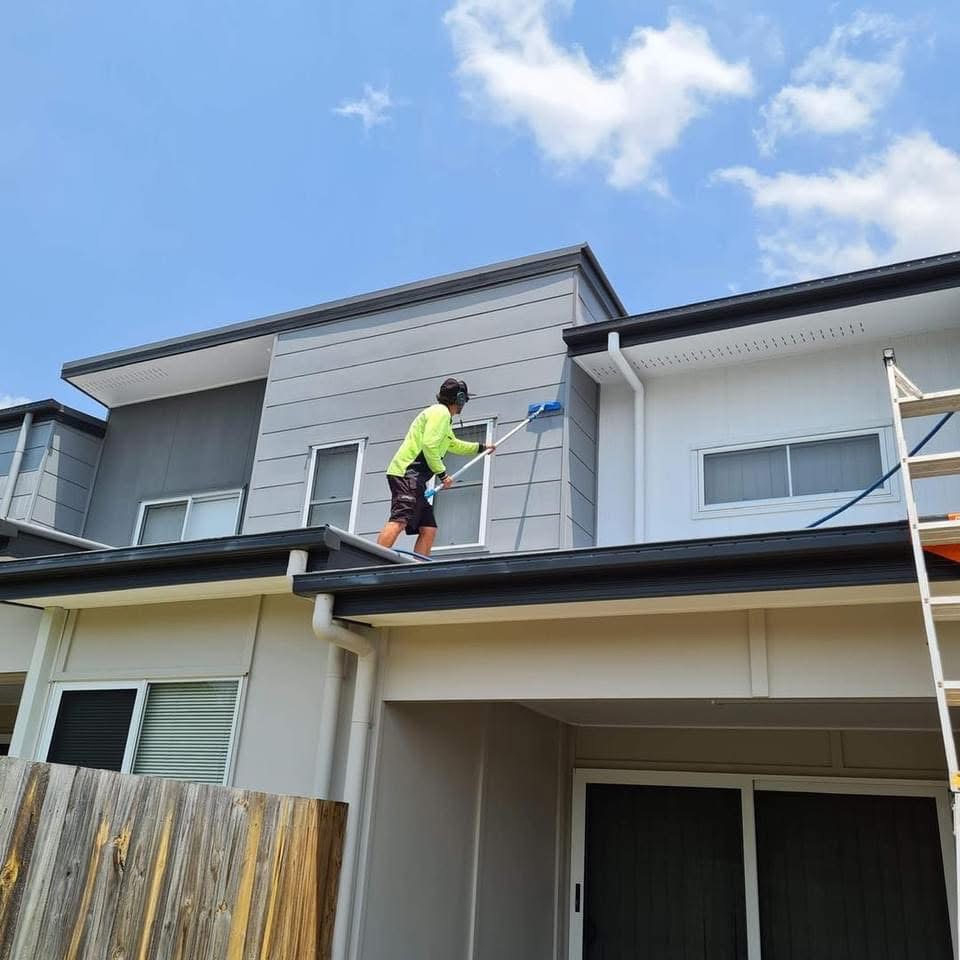 Michael paints a two-story house exterior on a roof under clouds, showing expert property maintenance in Brisbane Chermside West, Australia.