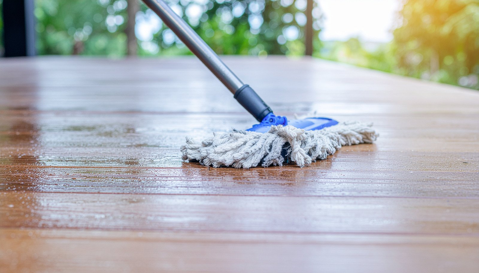 A mop cleaning a wet wooden floor outdoors with greenery, highlighting effective exterior mop cleaning.
